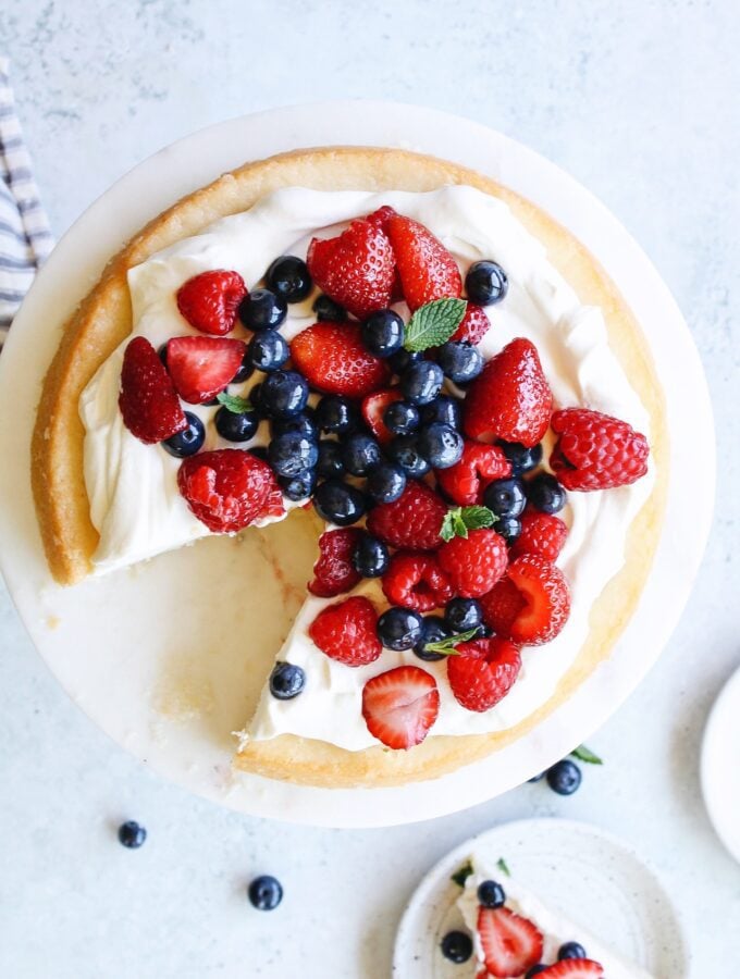 berries and cream cake on a white cake plate