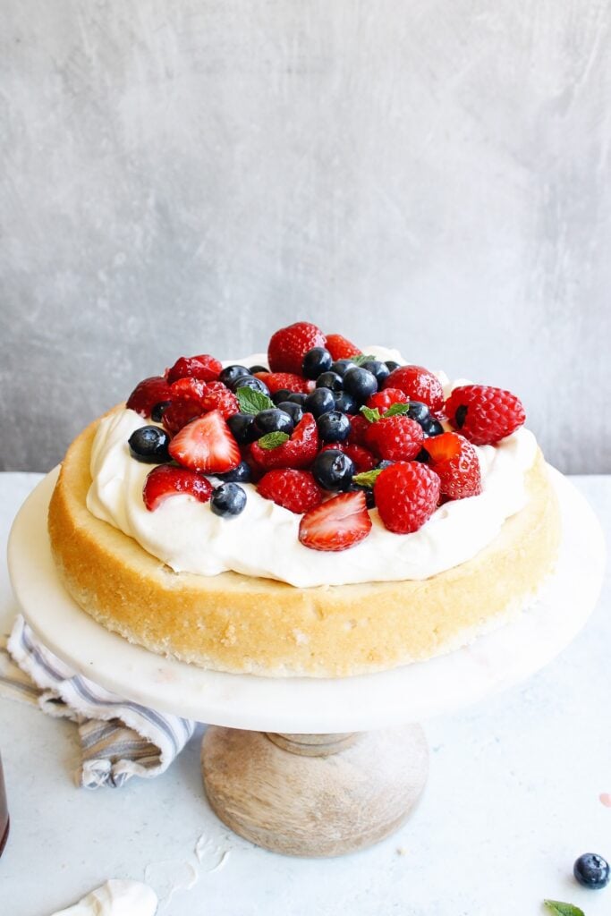 white cake topped with whipped cream and berries on a cake stand