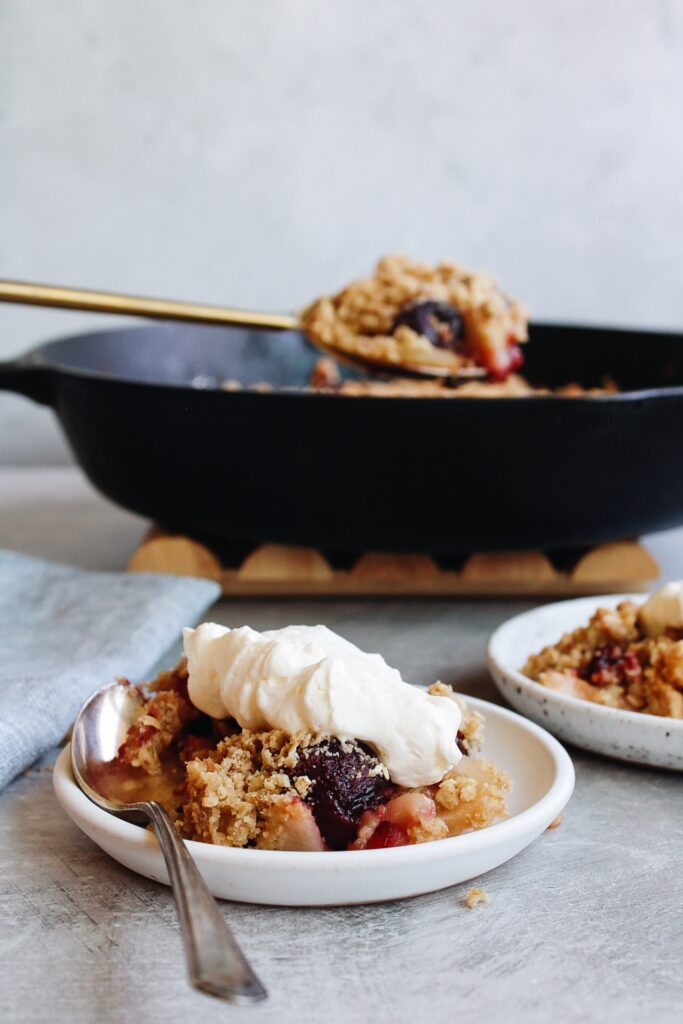 cherry apple crumble on a white plate with cast iron pan behind it