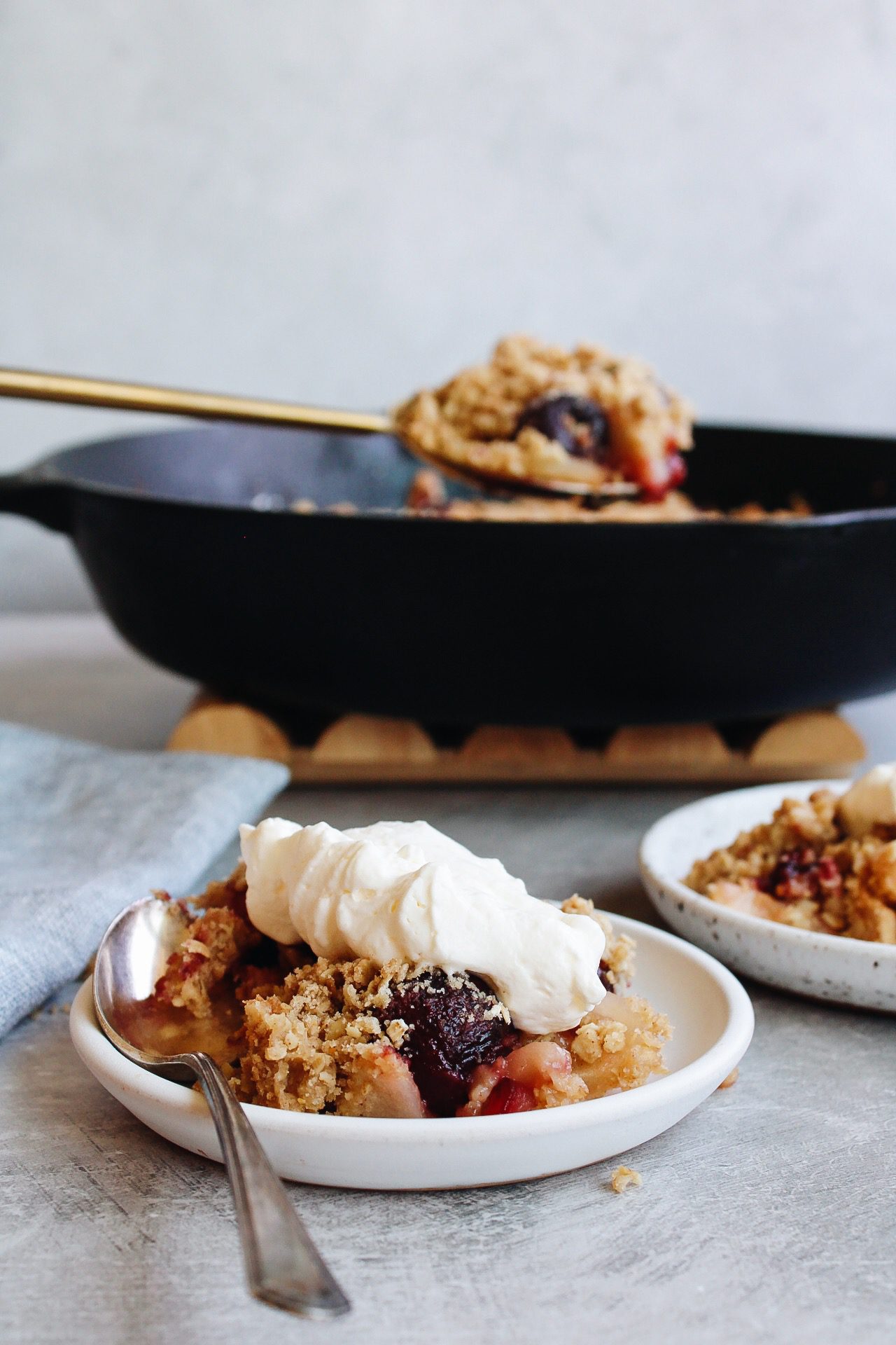 cherry apple crumble on a white plate with a cast iron skillet behind it