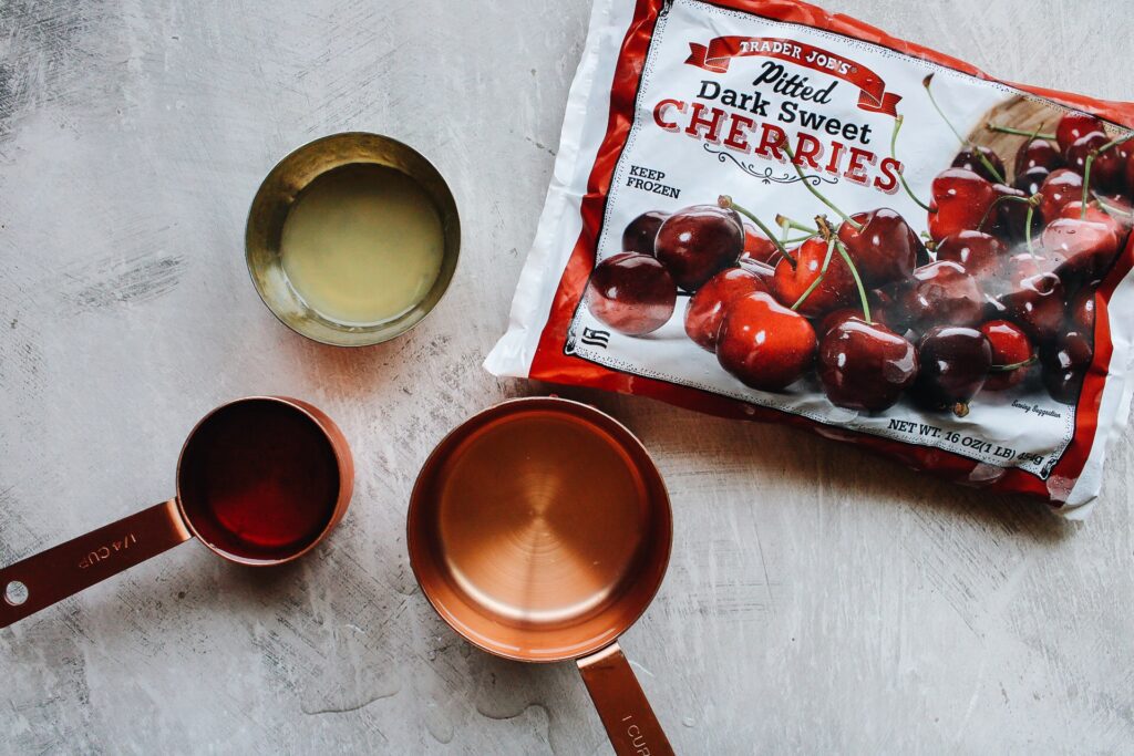 cherry popsicle ingredients: frozen cherries, lime juice, vanilla simple syrup and water on a gray background