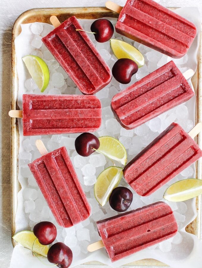 cherry popsicles on a tray with ice, limes and lime wedges