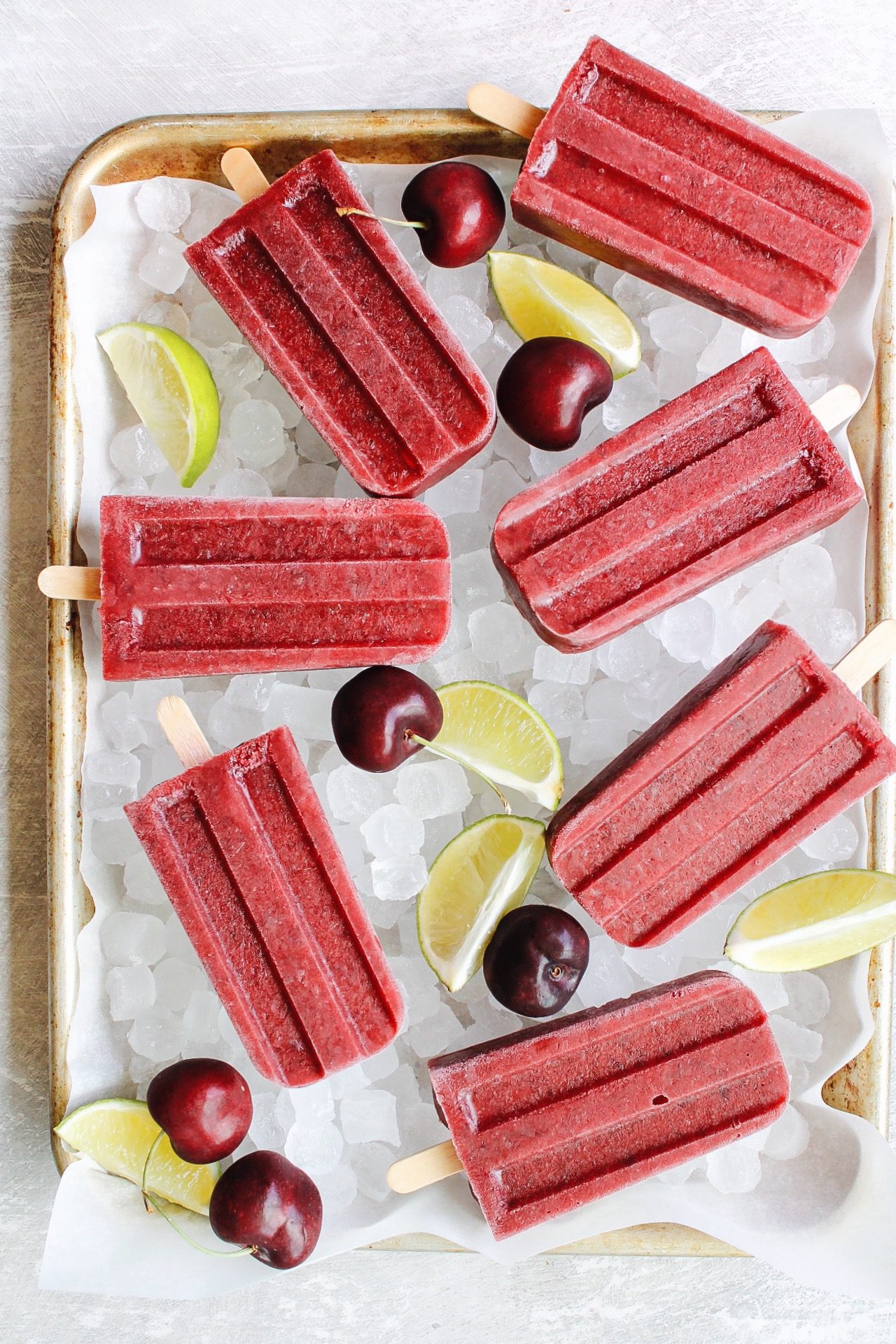 cherry popsicles on a tray with ice, lime wedges and cherries