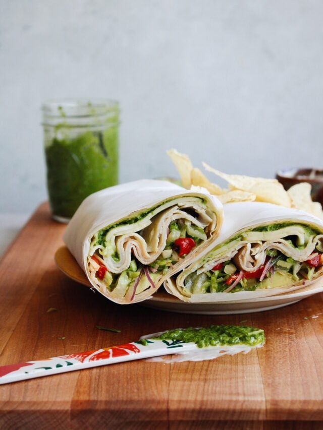 turkey pesto wrap cut in half and stacked on a plate with chips