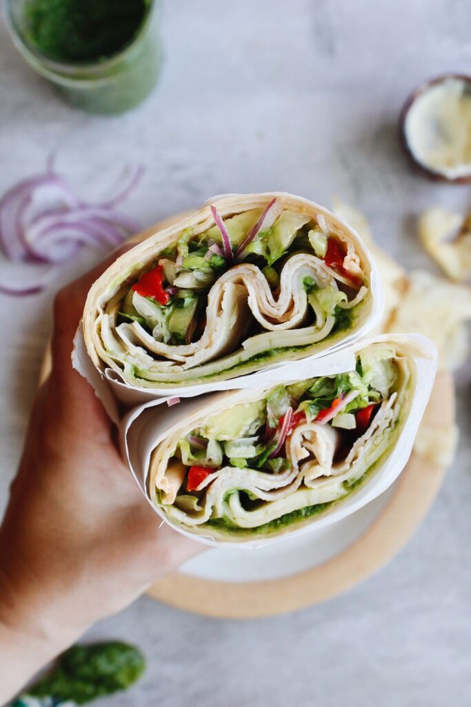 turkey pesto wrap cut in half being held in a hand