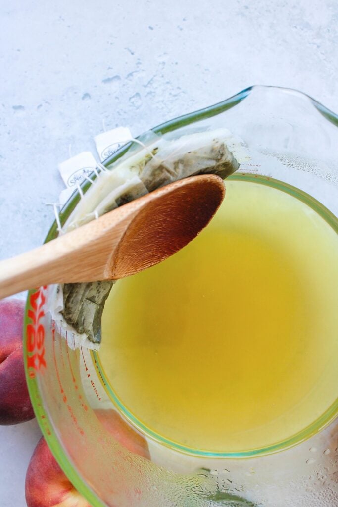 steeped green tea with a wooden spoon pressing tea bags against the side of the bowl