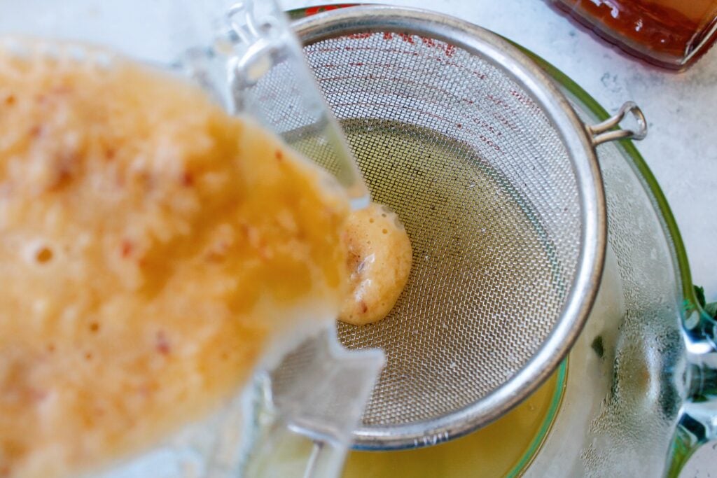 blended peaches being strained through a mesh sieve