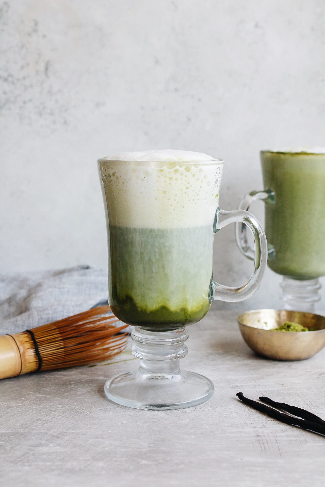 vanilla matcha latte in a clear glass with a matcha whisk next to it