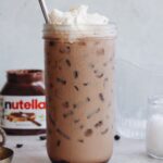 nutella latte in a clear glass with whipped cream on top