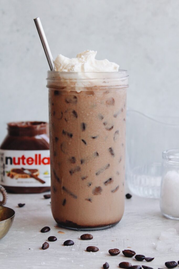 nutella latte in a clear glass with whipped cream on top