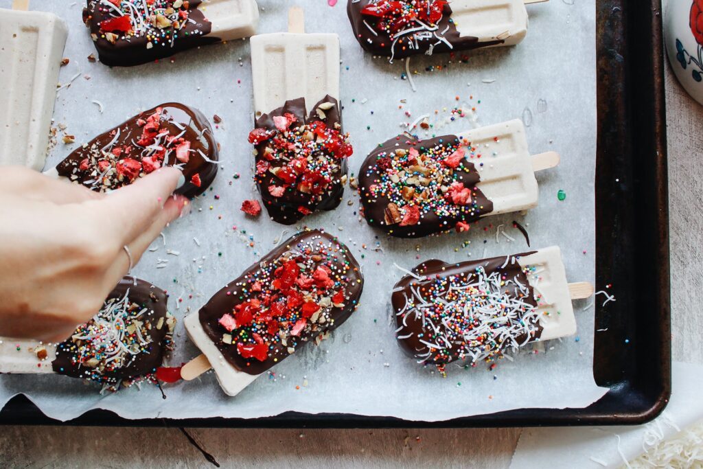 banana split tops on a parchment lined baking sheet getting toppings sprinkled on