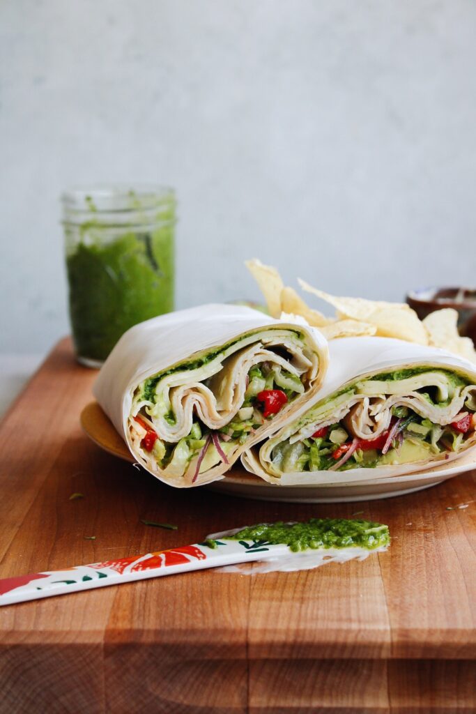 turkey pesto wrap cut in half and stacked on a plate with chips