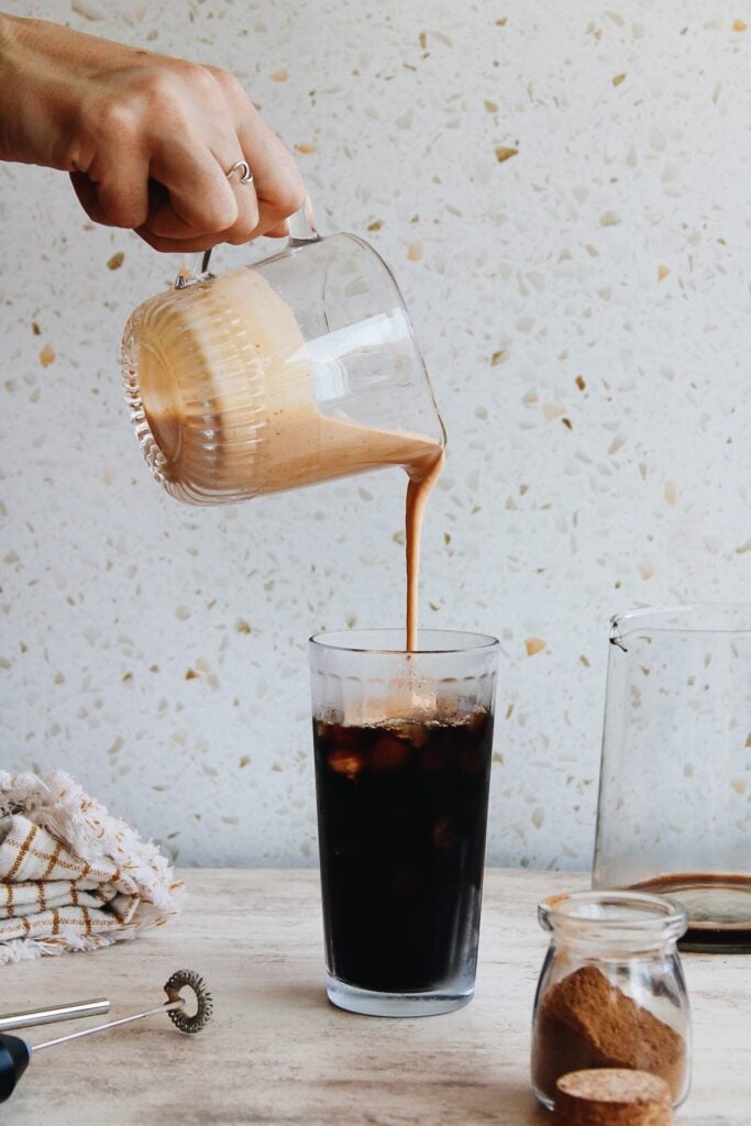 cold foam being poured on top of iced coffee