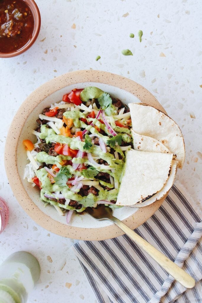 ground beef taco bowl with tortillas on the side and a striped napkin