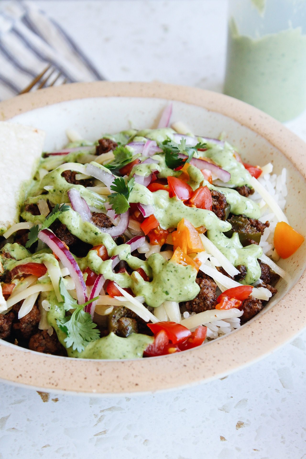 ground beef bowl topped with creamy cilantro sauce, tomatoes and pickled onion