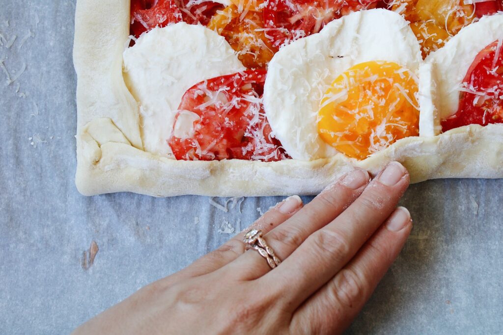 edge of puff pastry being folded up over sliced tomatoes and mozzarella