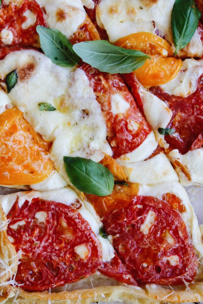 close up of puff pastry tomato tart topped with fresh basil