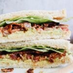 Close up of avocado BLT sandwich sliced in half and stacked on a plate