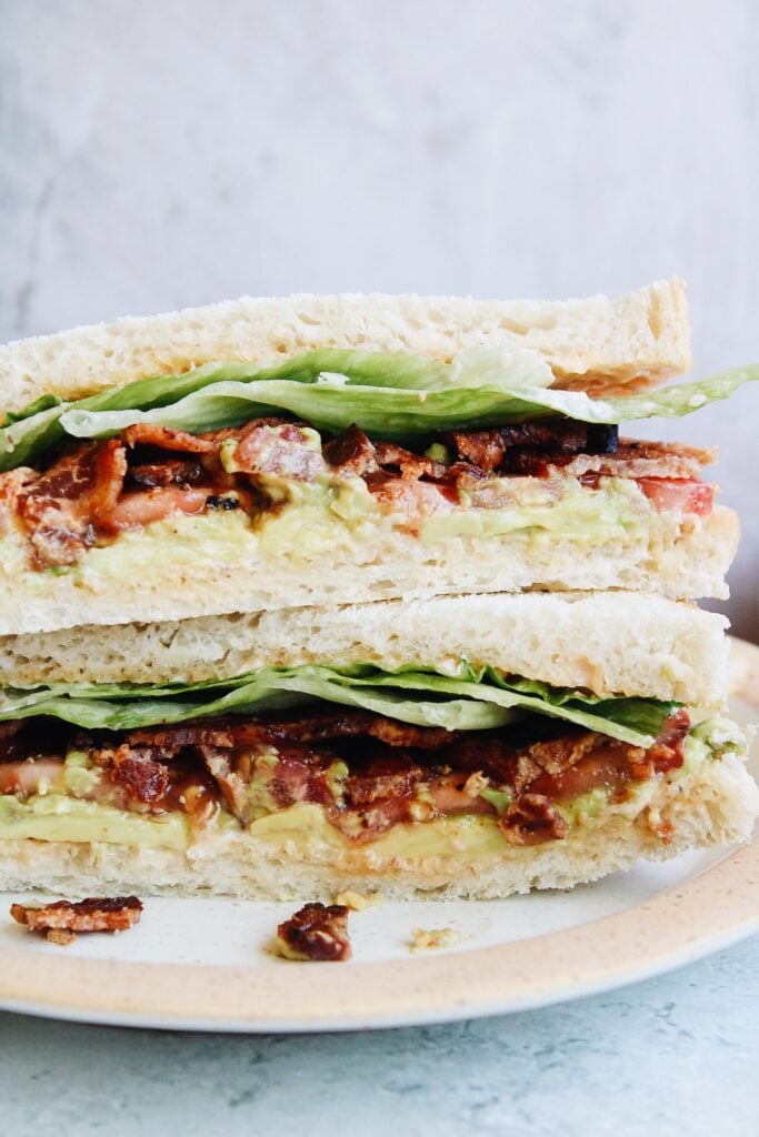 Close up of avocado BLT sandwich sliced in half and stacked on a plate 