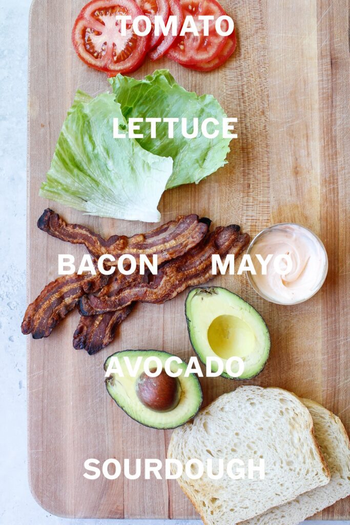 bacon, lettuce, avocado, ice berg lettuce, mayo and sourdough bread on a cutting board