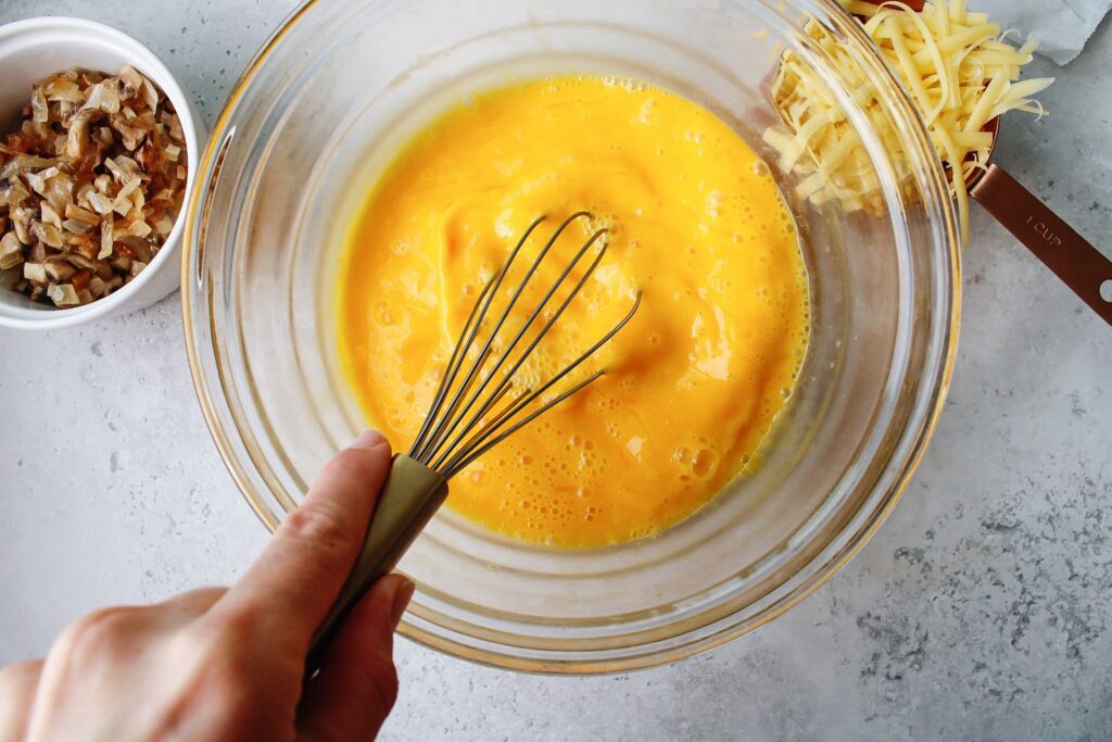 Eggs being beaten in a mixing bowl for bacon mushroom quiche 