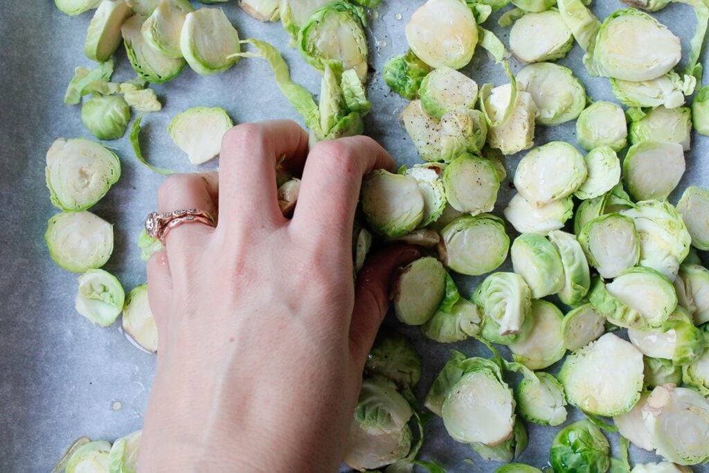 brussel sprouts being mixed with seasonings on a baking sheet