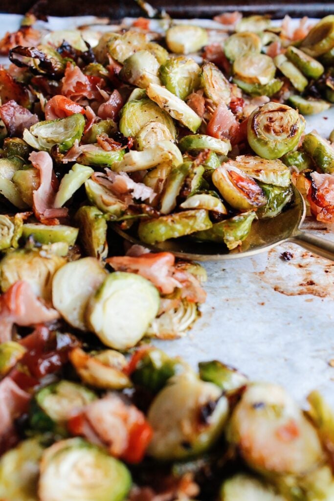 roasted brussel sprouts with prosciuto on a baking sheet with a gold spoon