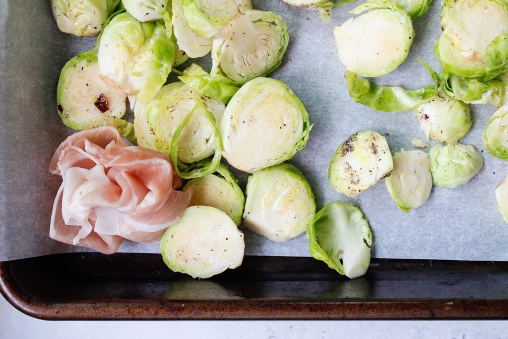 brussel sprouts on a baking sheet with clumps of prosciutto