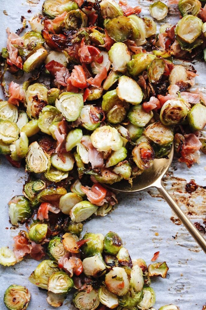 roasted Brussel sprouts with prosciutto on a baking sheet with a large golden serving spoon