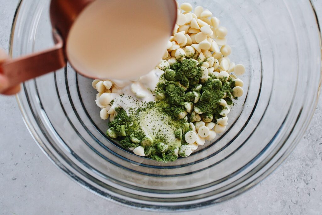 Heavy cream being poured into a bowl with white chocolate chips, matcha, salt and vanilla