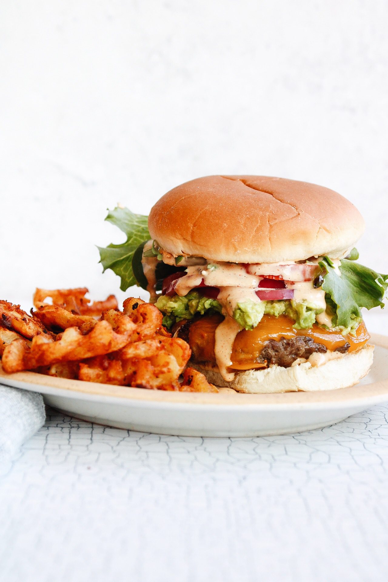 California burger with fries on a plate with a blue napkin next to it