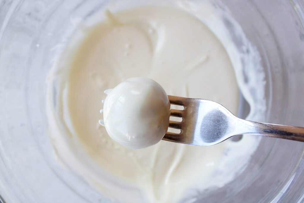 a matcha truffle ball being lifted out of melted white chocolate