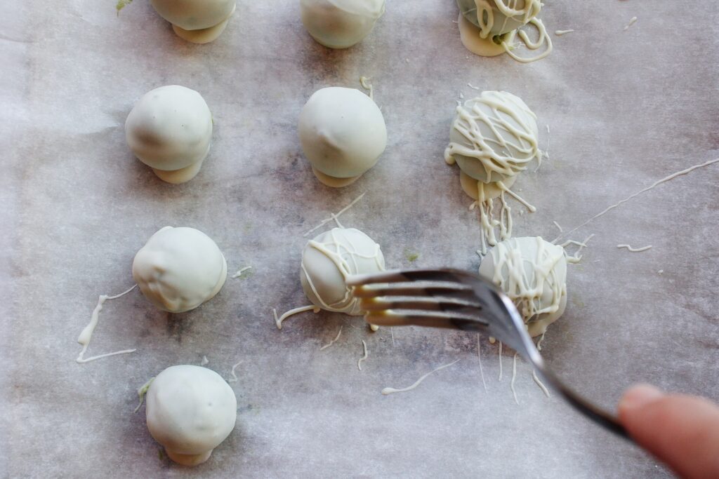 a fork being used to drizzle melted white chocolate over matcha truffles