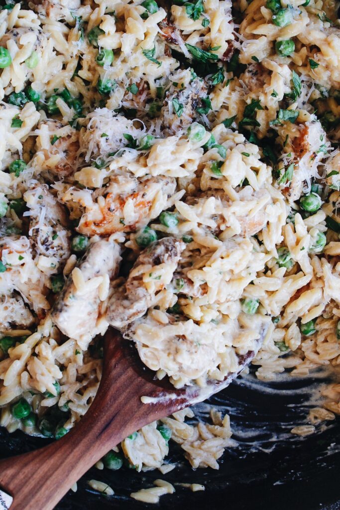 close up of boursin orzo with chicken and peas being scooped with a wooden spoon