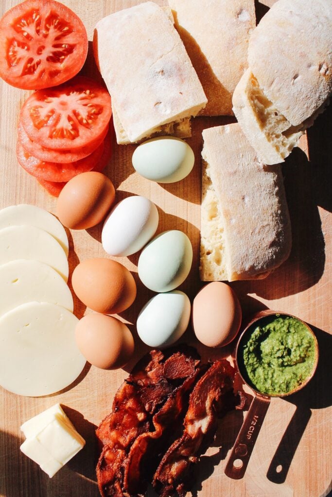 ingredients for pesto egg sandwiches on a wooden cutting board