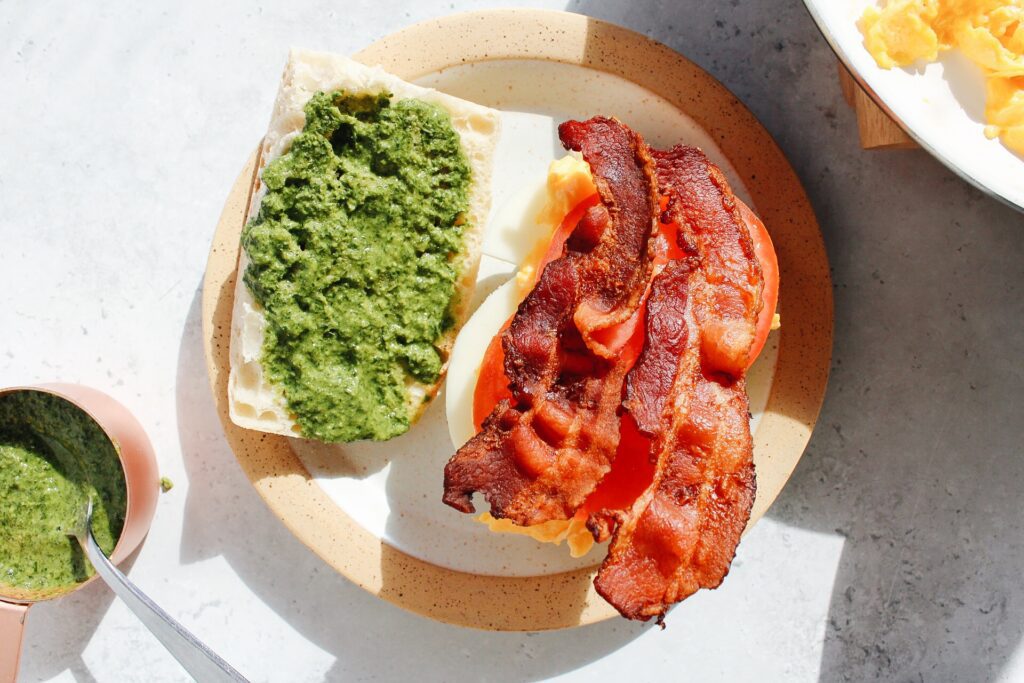 pesto egg sandwich being assembled on a plate with bacon