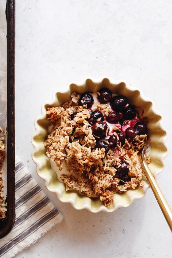 coconut cardamom granola in a small bowl topping yogurt with blueberries