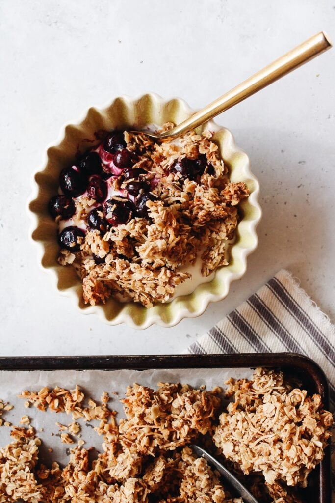 coconut cardamom granola in a bowl topping yogurt with blueberries