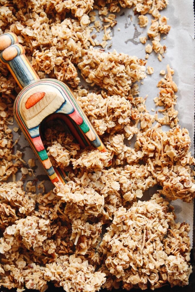 cardamom granola on a baking sheet with a rainbow colored scoop