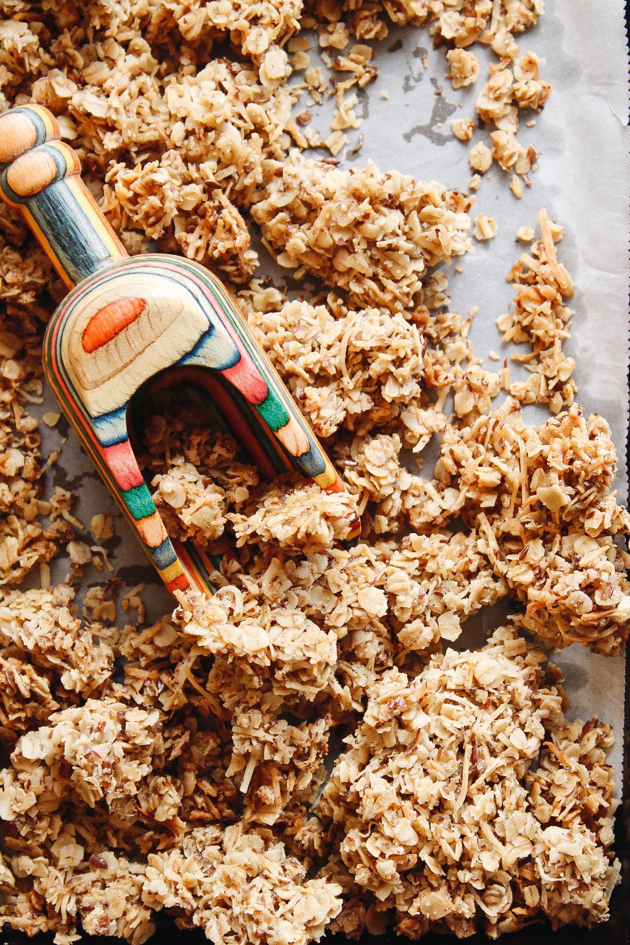 cardamom granola on a baking sheet with a rainbow colored scoop