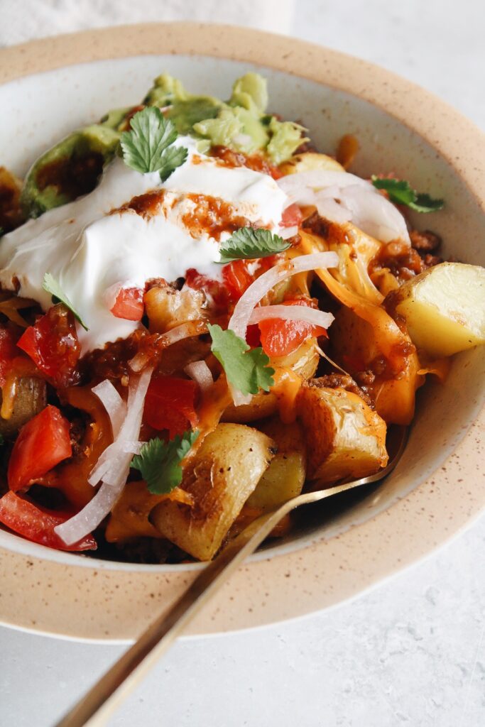 potato taco bowl topped with sour cream, guacamole, tomatoes and pickled onions