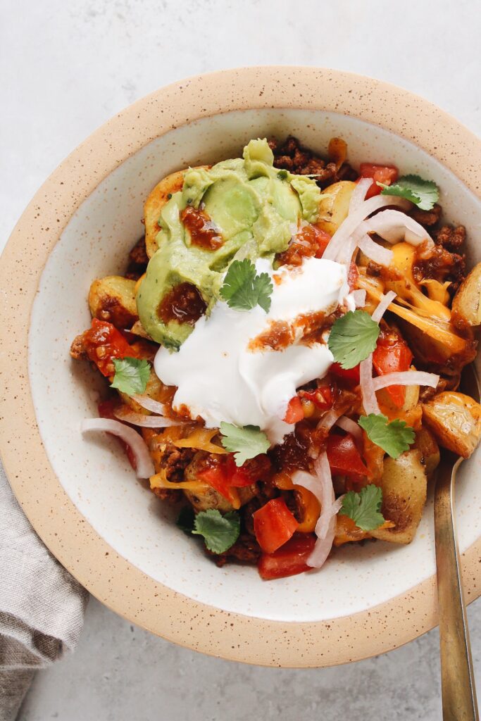 easy potato taco bowl topped with guacamole and sour cream