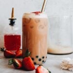 strawberry bubble tea in a clear boba glass topped with strawberries