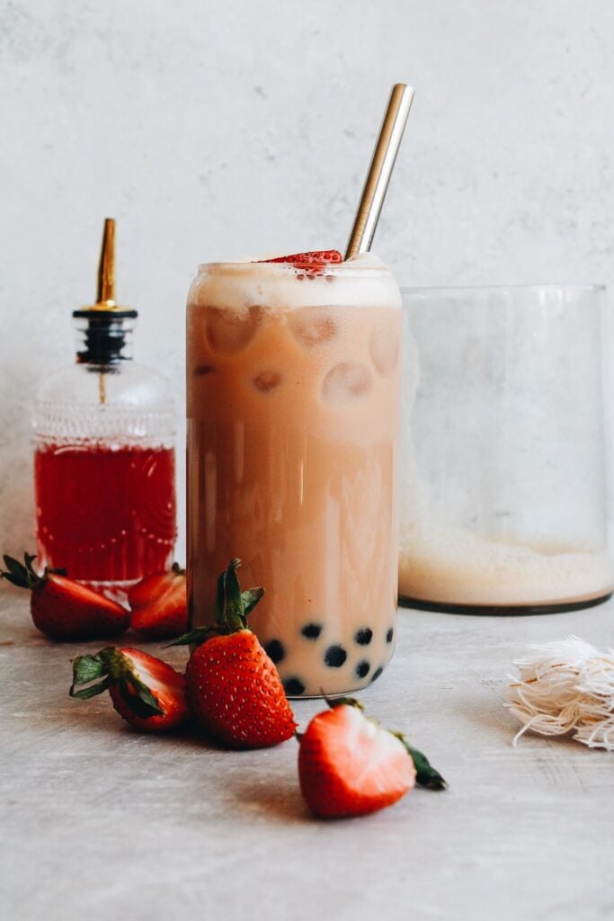 strawberry bubble tea in a clear boba glass topped with strawberries